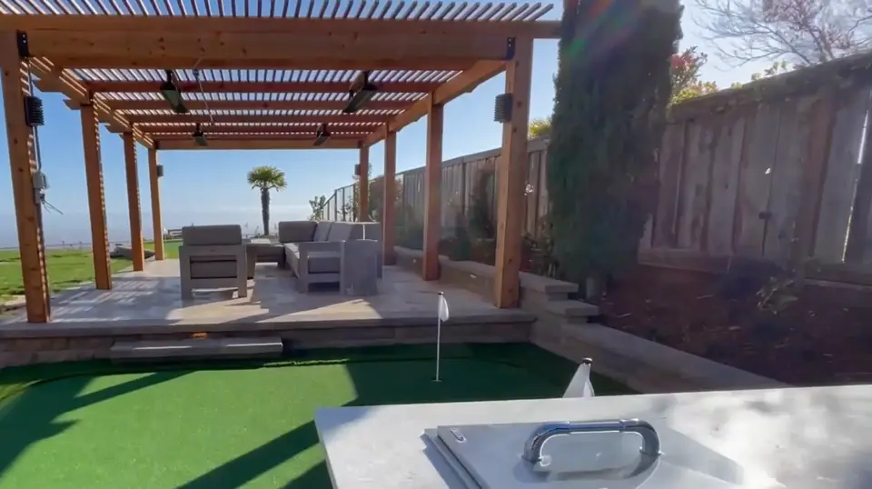 Turf putting green beside a pergola and outdoor kitchen